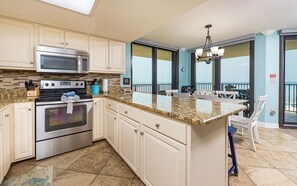 A kitchen with a large island, stainless steel appliances, and a view of the ocean through the windows. - Phoenix East 511 3 Bedroom Condo (Orange Beach)