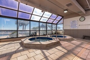 A spa area with two hot tubs, large windows offering a view of palm trees and a beach, and a sign detailing spa rules. - Phoenix East 511 3 Bedroom Condo (Orange Beach)