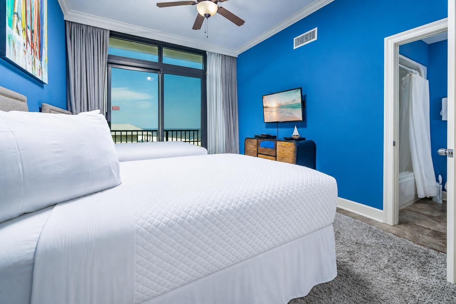 A hotel room with a large bed, a ceiling fan, a television, and a view of the outdoors.