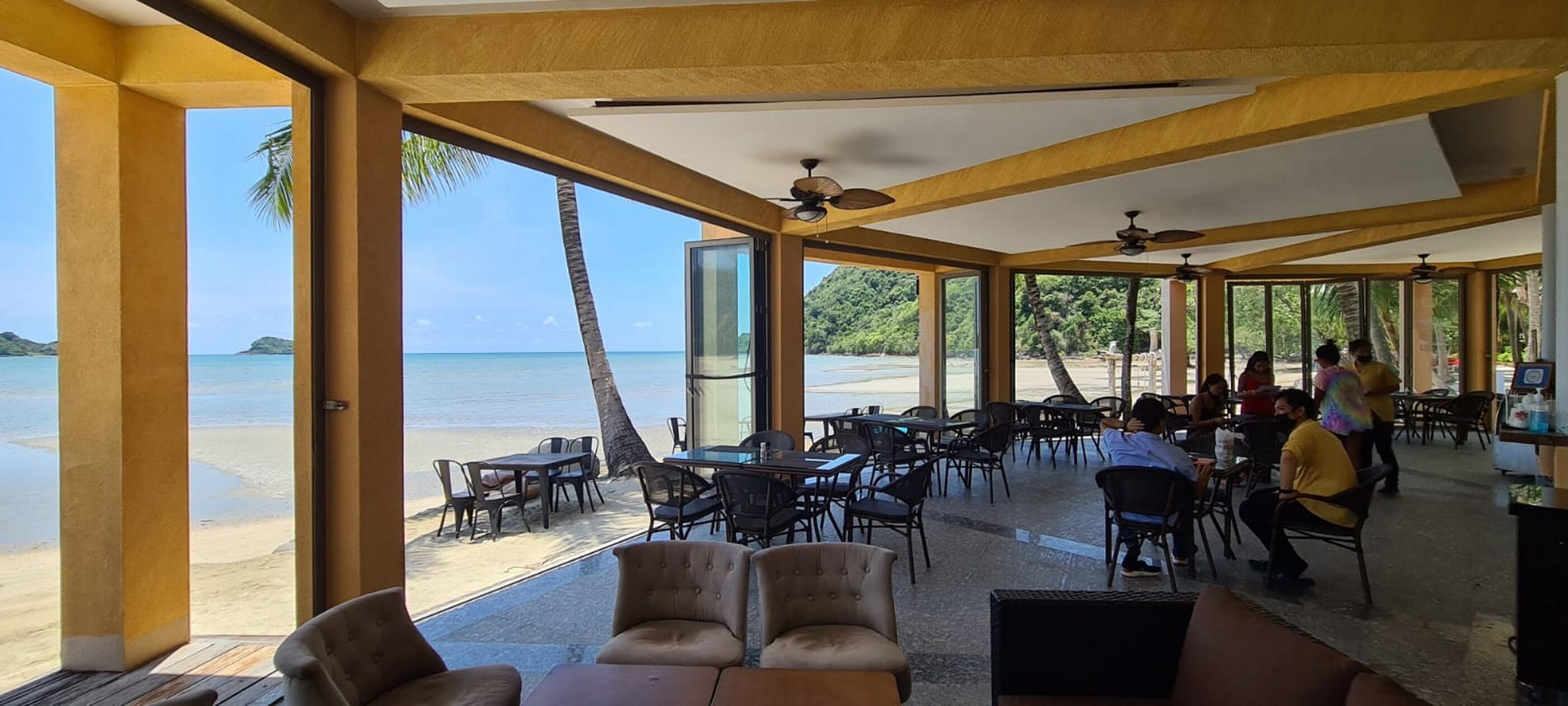 A covered outdoor seating area with tables and chairs, overlooking a beach and ocean.