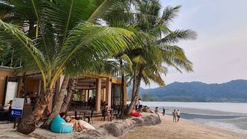 A beachside cafe with outdoor seating, palm trees, and a view of the sea.
