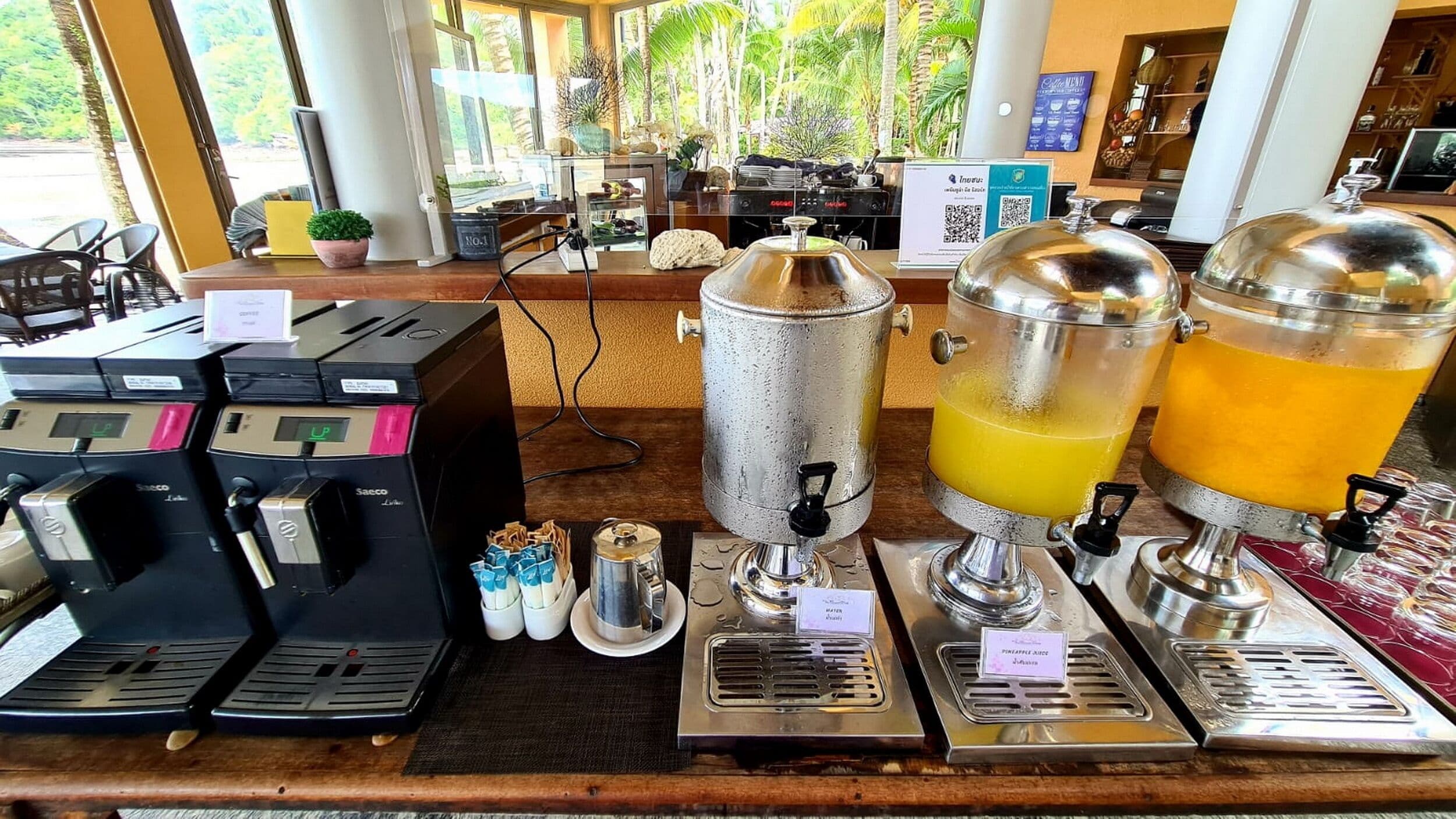 A coffee station with multiple espresso machines, a water dispenser, and two fruit juice dispensers.