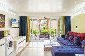 Een moderne woonkamer met een bank, een televisie, een wasmachine en een eethoek met stoelen en een tafel.