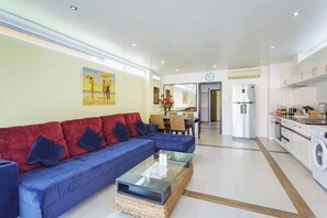 A modern living room with a sectional sofa, a glass coffee table, and a dining area with a table and chairs. - 1 Bedroom Beach Villa Apartment (Ko Chang)