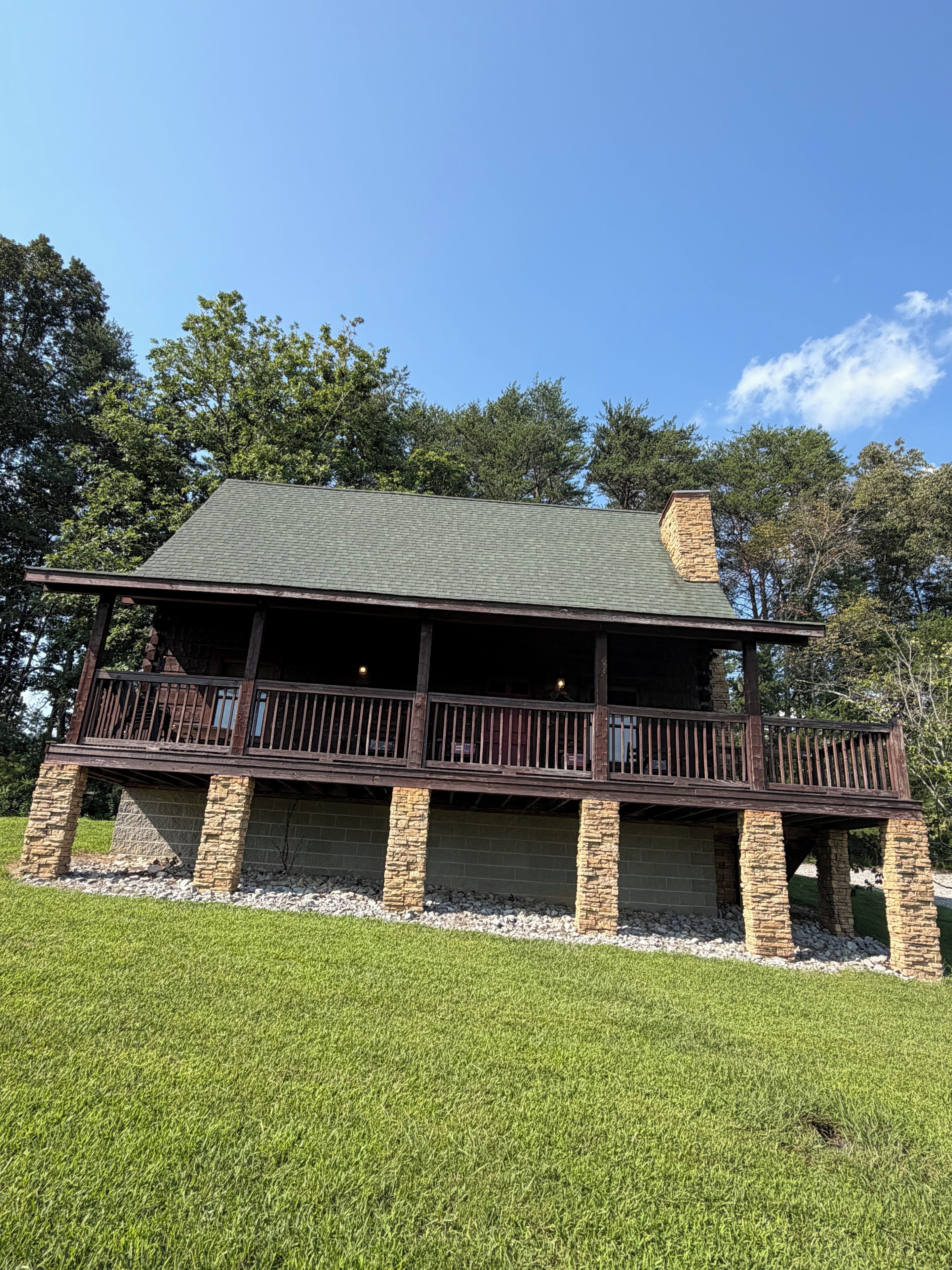 A two-story house with a balcony, stone foundation, and a green roof.