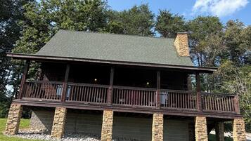 A two-story house with a balcony, stone foundation, and a green roof.