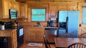 Cocina estilo cabaña de madera con una isla central, armarios de madera, refrigerador de acero inoxidable y una mesa de comedor con sillas.