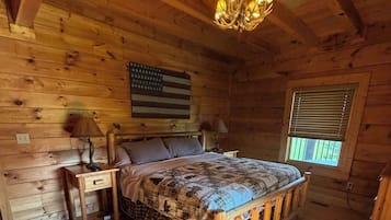 A wooden cabin bedroom with a bed, two nightstands, a ceiling fan, and a window with blinds.