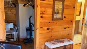Un interior de madera con un banco, un armario con ropa colgada y una aspiradora.