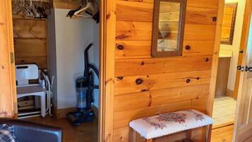 A wooden interior with a bench, a closet with hanging clothes, and a vacuum cleaner.
