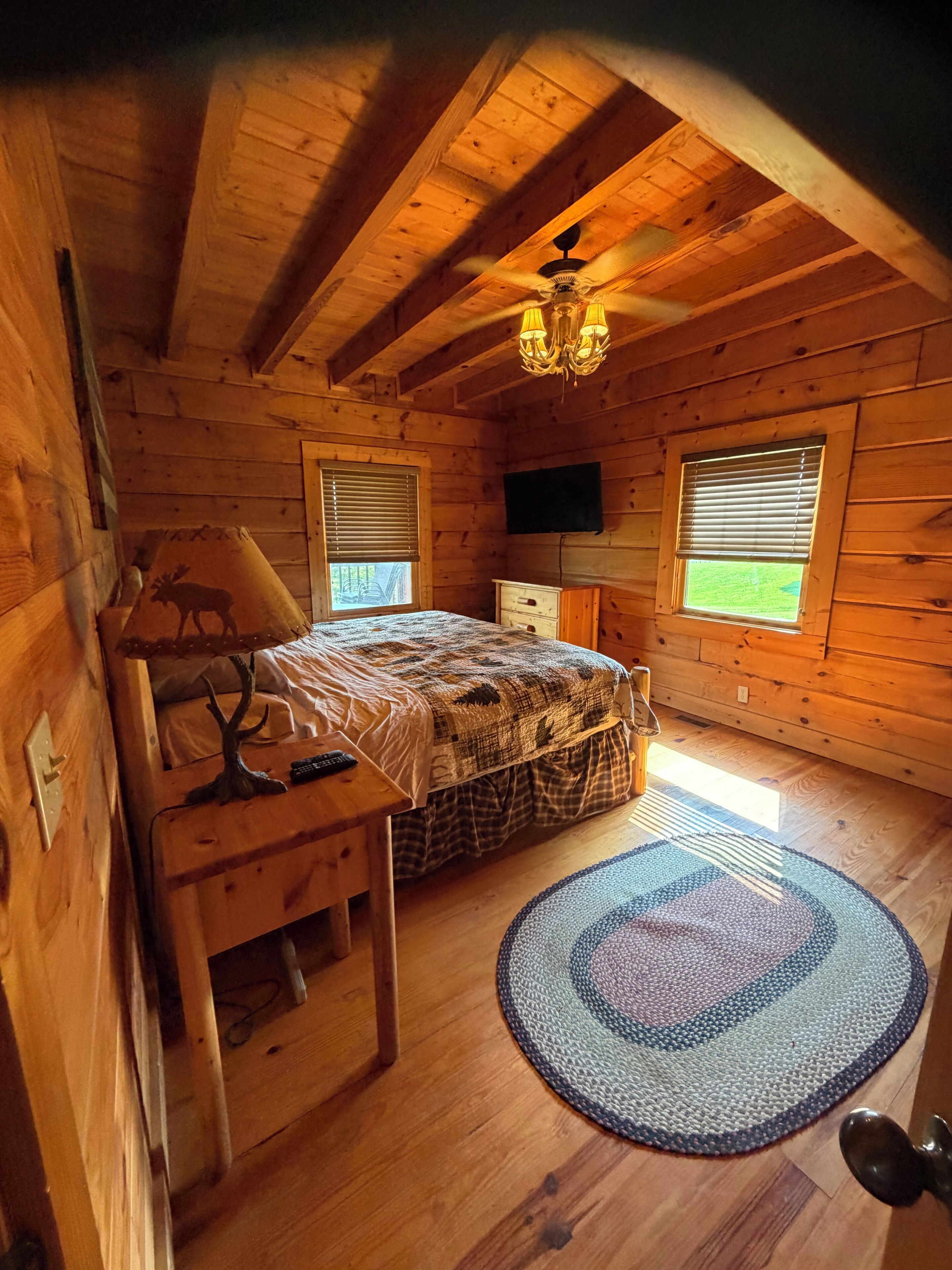 Een slaapkamer in een houten chalet met een bed, een bureau, een stoel, een televisietoestel en een raam.