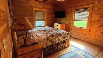 Une chambre dans un chalet en bois, avec un lit, un bureau, une chaise, une télévision et une fenêtre.