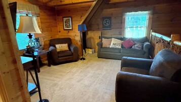 A cozy cabin interior with a ceiling fan, two sofas, a table, and a window with blinds.