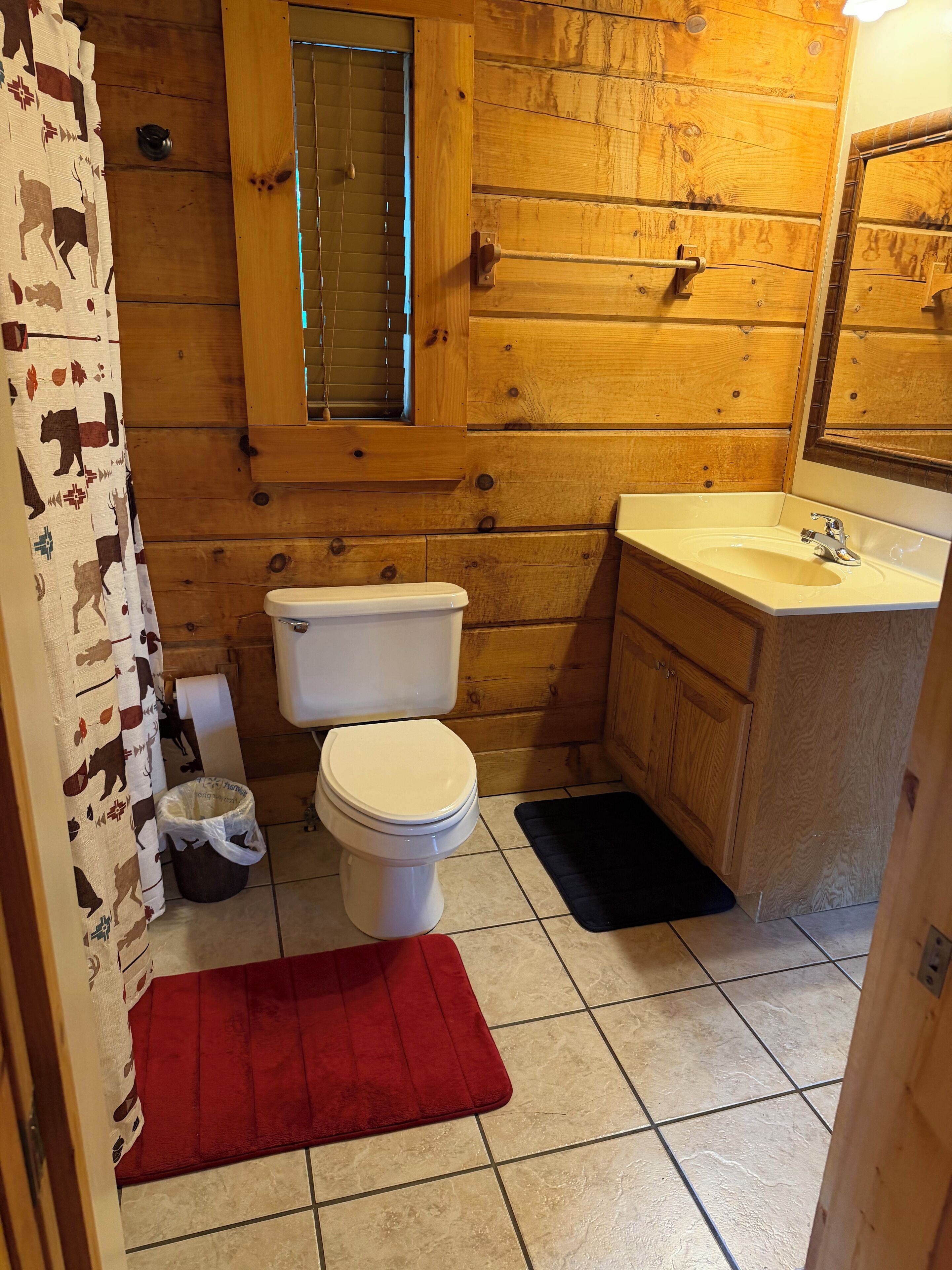Ein Badezimmer einer Holzhütte mit Toilette, Waschbecken und einem Fenster über der Toilette.