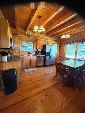 Interior de una cabaña de madera con zona de cocina que incluye refrigerador, estufa y armarios de madera.