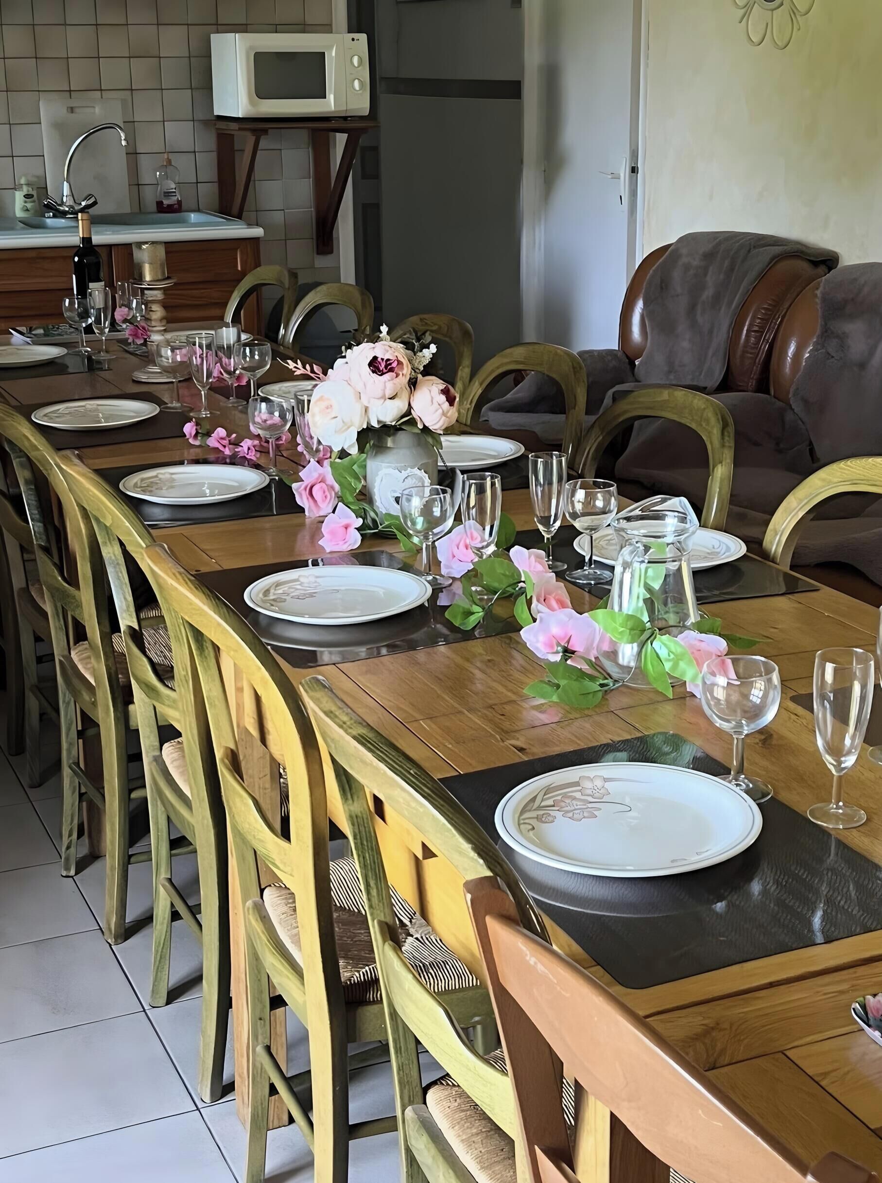 Mesa de jantar posta para seis lugares, com cadeiras, um vaso de flores e um micro-ondas ao fundo.
