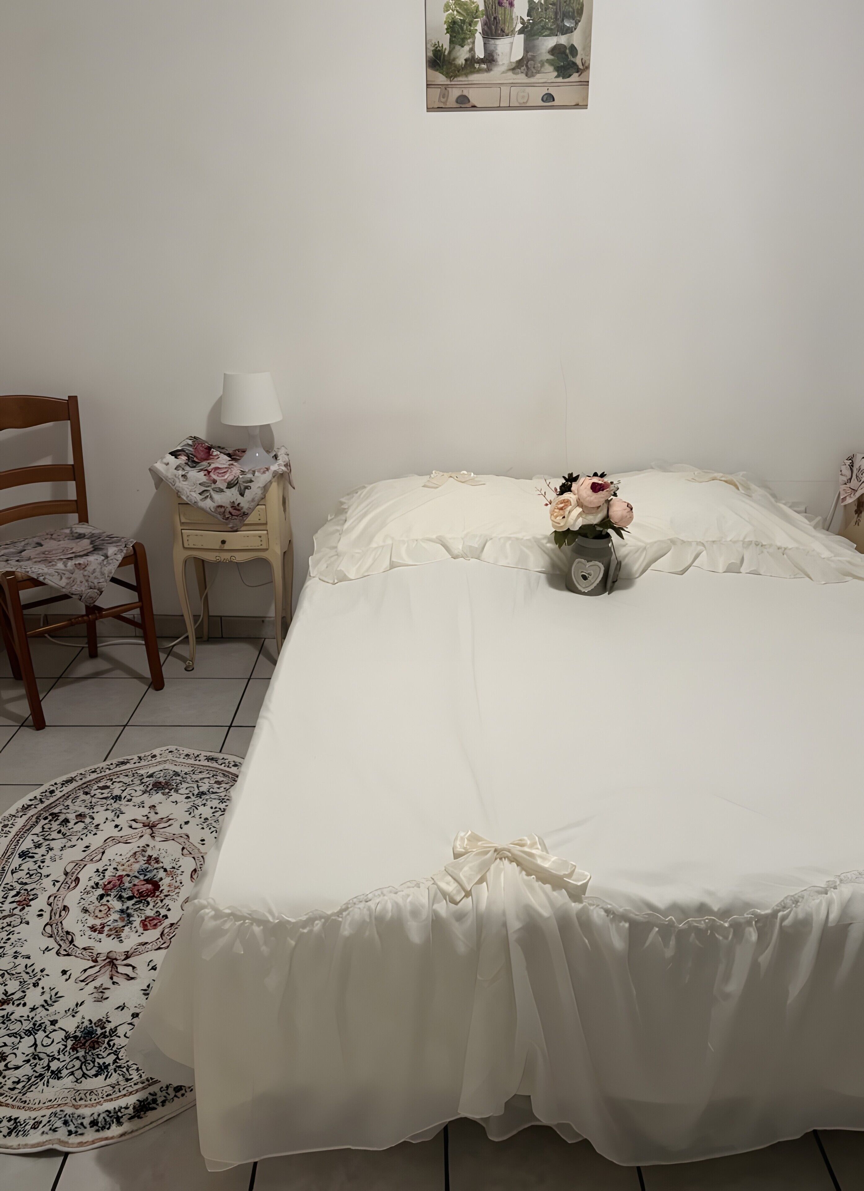 Un dormitorio con cama, una silla, una mesita de noche, una lámpara y una alfombra con estampado floral.