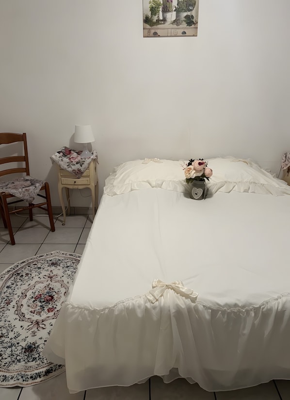 A bedroom with a bed, a chair, a nightstand, a lamp, and a floral-patterned rug.