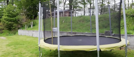 A trampoline with a safety net, surrounded by grass and trees.