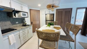 Una cocina moderna con armarios blancos, un refrigerador de acero inoxidable y un microondas. Cuenta con una mesa de comedor con sillas de mimbre y un ventilador de techo.