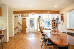 Una àmplia zona de menjador amb taula i cadires de fusta, una escala que condueix a una altra habitació, i vistes a l'exterior a través d'una porta de vidre.