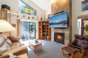 Ein modernes Wohnzimmer mit Kamin, Fernseher und großem Fenster.