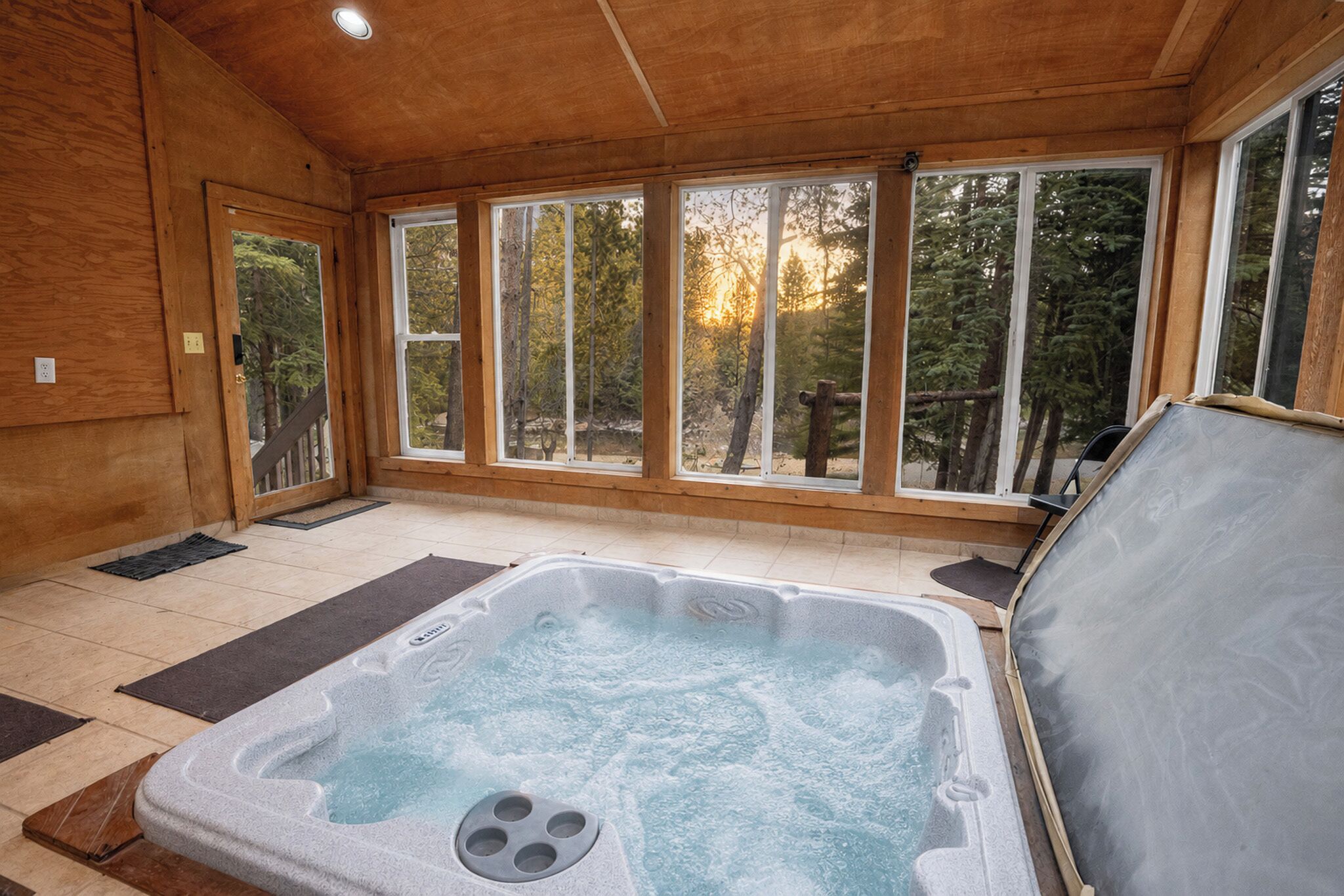 A spa room with a hot tub, wooden walls, and large windows.