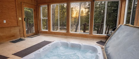 A spa room with a hot tub, wooden walls, and large windows.