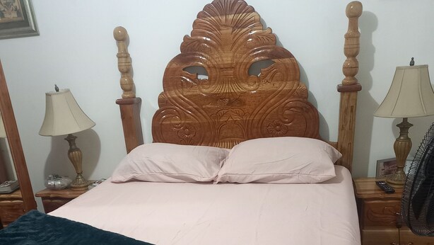 A bedroom with a wooden headboard, a bed with a white and dark blue bedspread, two bedside tables with lamps, and a nightstand with a lamp. - COLDEST 1-bedroom apartment with AC in serene Montego Bay (Montego Bay)