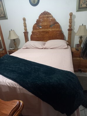 A bedroom with a wooden headboard, a bed with a white and dark blue bedspread, two bedside tables with lamps, and a nightstand with a lamp. - COLDEST 1-bedroom apartment with AC in serene Montego Bay (Montego Bay)