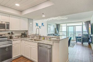 A modern kitchen with white cabinets, stainless steel appliances, and a marble countertop. - Carolinian Beach Resort Penthouse 32 (Myrtle Beach)