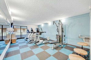 A gym with cardio machines, a mirror, and a small seating area with stools. - Carolinian Beach Resort Penthouse 32 (Myrtle Beach)