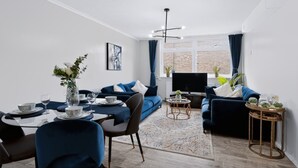 A modern living room with a sofa set, a dining table with chairs, a TV, and a window with curtains. - 2 Bed 1 Bath Apt in Fulham in Zone 2 (London)