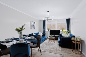 A modern living room with a sofa set, a dining table with chairs, a TV, and a window with curtains. - 2 Bed 1 Bath Apt in Fulham in Zone 2 (London)