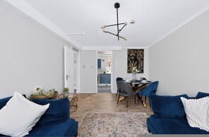 A modern living room with a dining area, a kitchen in the background, and a hallway leading to an open space. - 2 Bed 1 Bath Apt in Fulham in Zone 2 (London)