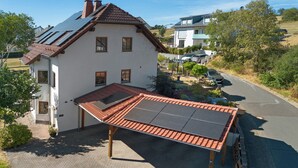 Ein zweistöckiges Haus mit geneigtem Dach, einer überdachten Terrasse und Solaranlage sowie einer gepflasterten Auffahrt.