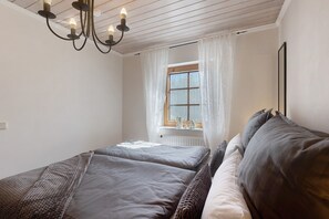 A bedroom with two beds, a window with curtains, a radiator, and a chandelier.
