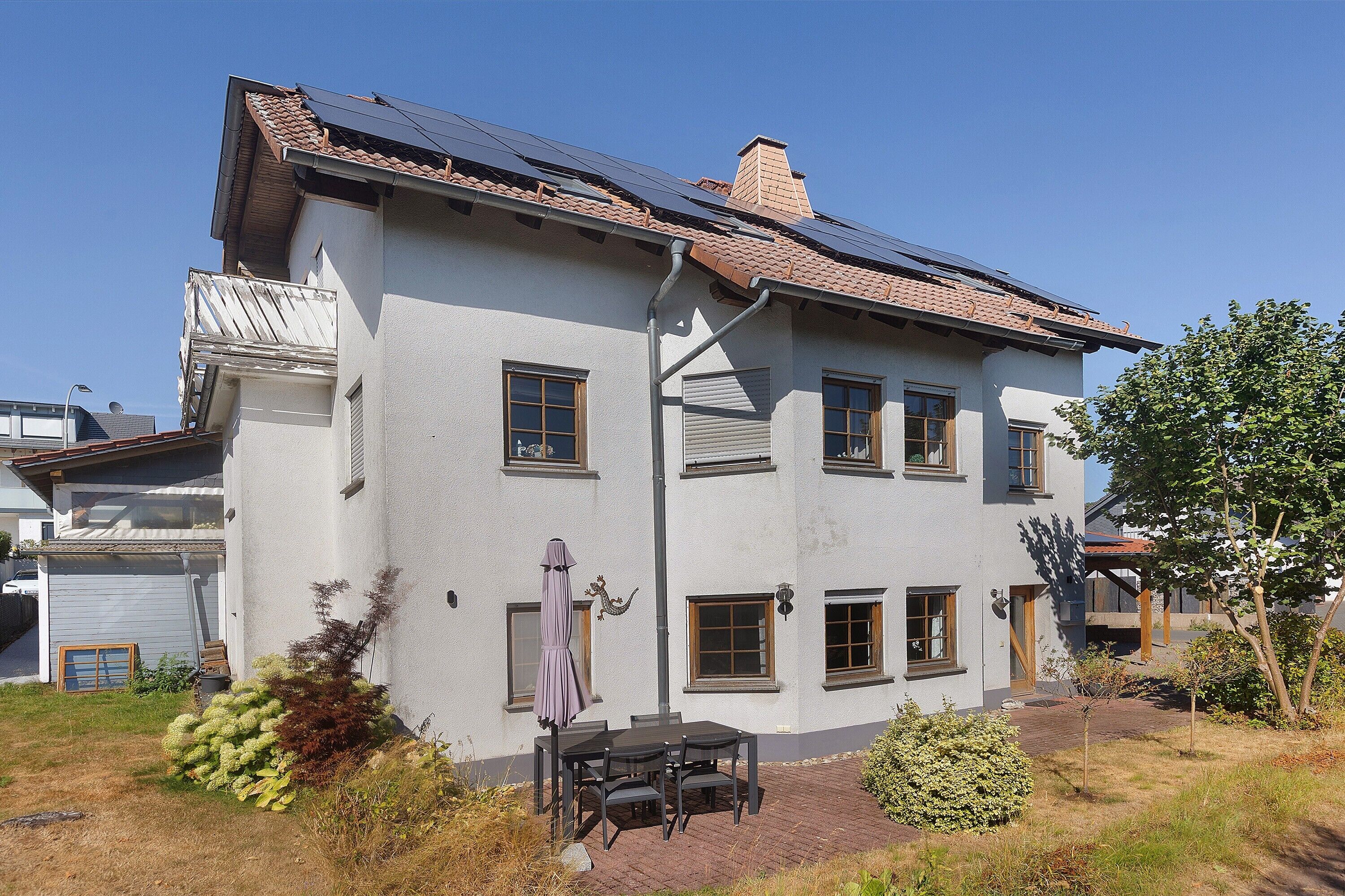A two-story house with a tiled roof, multiple windows, and a patio area with outdoor furniture.