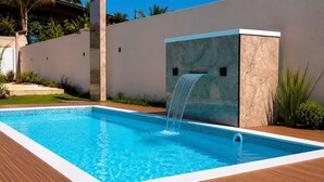 Et rektangulært swimmingpool med et vandfald, omgivet af en træterrasse og en lav mur.