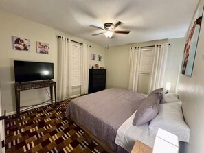 Ein Schlafzimmer mit Bett, Fernseher, Deckenventilator und Kommode.