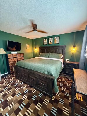 A bedroom with a bed, a ceiling fan, a TV, and a patterned floor. - Crowders Cozy Retreat (Gastonia)
