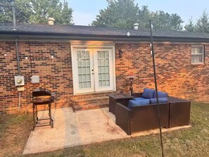 Ein Backsteinhaus mit Terrasse, Grill und einem Korbsesselsofa.