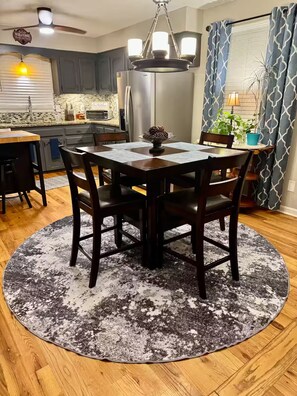A dining area with a round table, chairs, a chandelier, and a kitchen in the background.