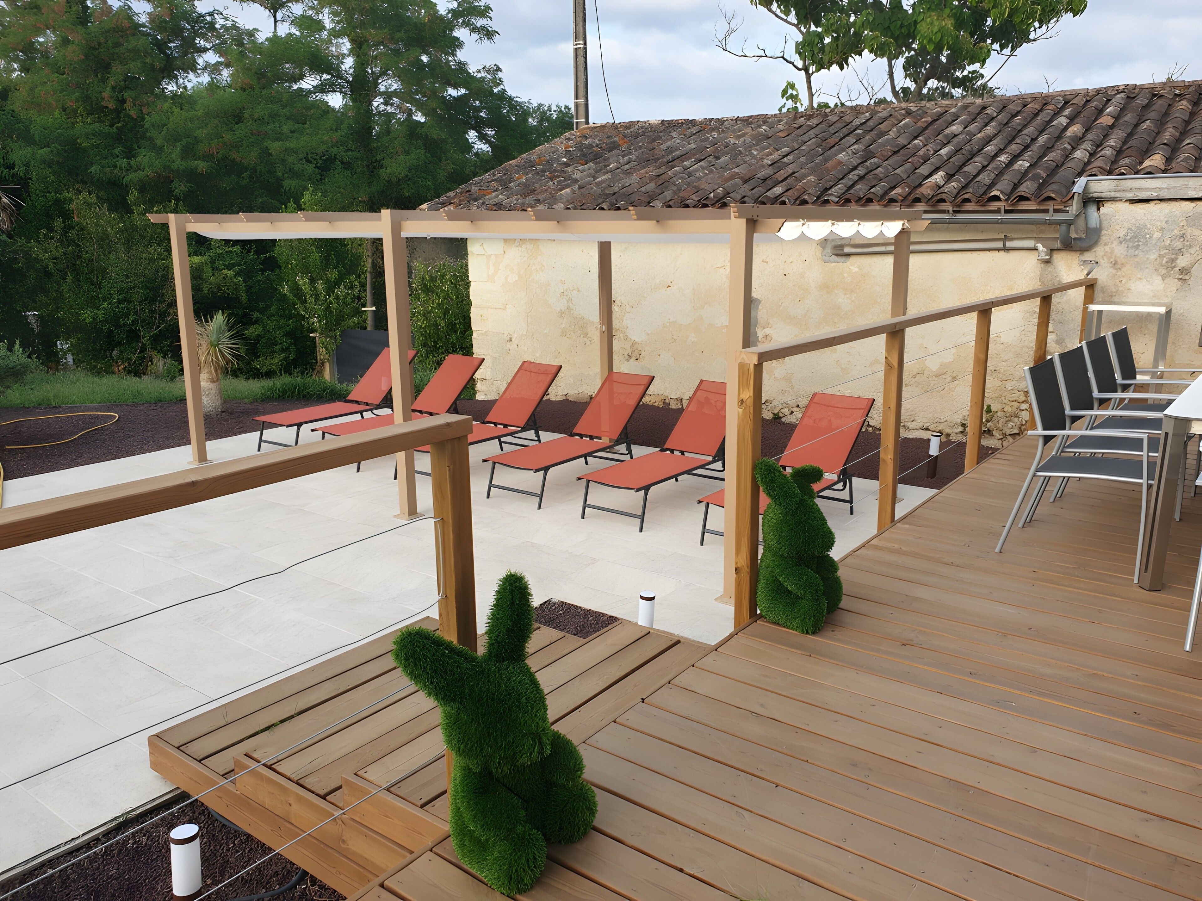An outdoor patio with wooden flooring, a pergola, and red lounge chairs.