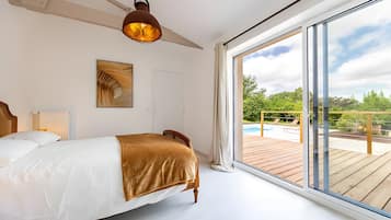 A bedroom with a large bed, a ceiling fan, a painting, and a view of an outdoor pool area.