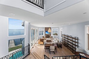 Un amplio salón con vistas al mar, chimenea y una escalera moderna.