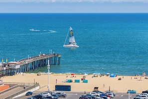 A pier extending into the ocean with a sailboat in the distance, a beach with people and umbrellas, and a parking lot with cars. - Azure Bay Retreat (Ocean City)
