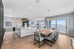 Una cocina moderna con una isla central, comedor con sillas y ventanas amplias con vista al agua.