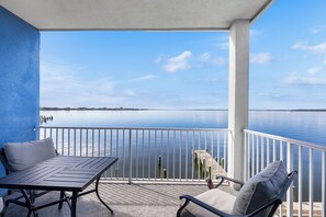 A balcony with a table and chairs, overlooking a calm body of water and a distant shoreline. - Azure Bay Retreat (Ocean City)