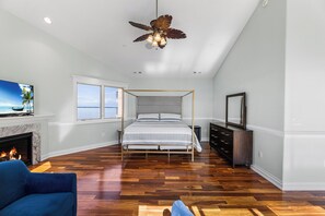 Une chambre à coucher avec un lit à baldaquin, un ventilateur de plafond, une cheminée et une grande fenêtre donnant sur la mer.